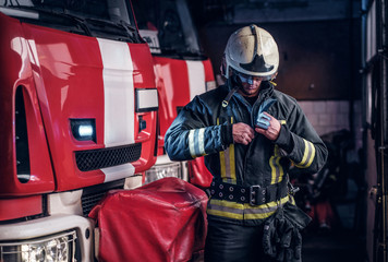Fototapeta premium Fireman clothes protective uniforms standing next to the fire engine in the garage of a fire department