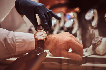 Assistant helps the client to try on exclusive men's watches, close-up hands.