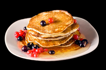 Pancakes with honey and currant. Black background. Selective focus.