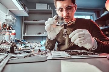 Electronic technician mending a broken tablet carefully examines the chip of the tablet using a...