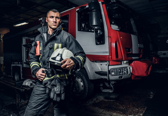 Fireman wearing uniform holding a helmet and looking at a camera while standing near a fire truck...