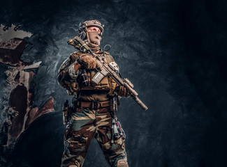 Special forces soldier in military uniform posing with assault rifle. Studio photo against a dark textured wall