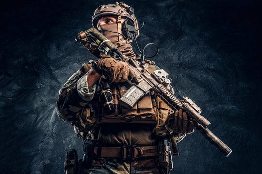 Elite unit, special forces soldier in camouflage uniform posing with assault rifle. Studio photo against a dark textured wall