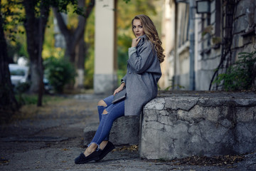 Fashion model wearing ripped boyfriend jeans, jacket and sneakers posing in the city