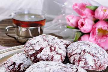 Red cracked cookies covered with white icing sugar on a silver old tray next to a cup of green tea in a glass cup with a silver cup holder