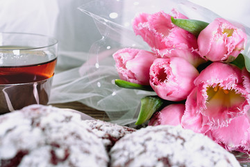 A bouquet of pink tulips on the background of cookies and a cup of tea