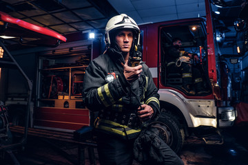 The fire brigade arrived at the night-time. Fireman in a protective uniform standing next to a fire truck and talking on the radio