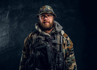 Portrait of a special forces soldier in the military camouflaged uniform, looking at a camera. Studio photo against a dark textured wall