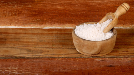 Salt or sea salt in a wooden bowl on a aged wooden table background.