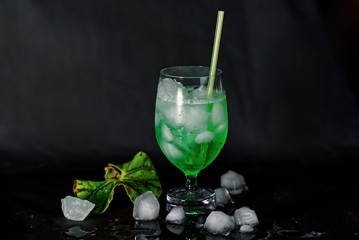Green drink, cocktail with ice next to glass on black background