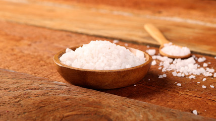 Salt or sea salt in a wooden bowl on a aged wooden table background.