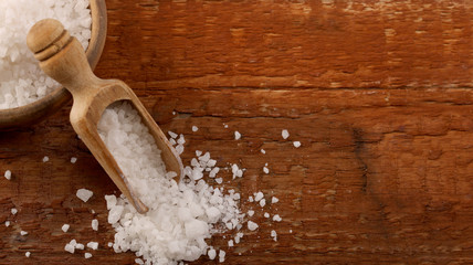 Top view of Salt or sea salt in a wooden bowl on a aged wooden table background.