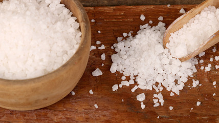 Salt or sea salt in a wooden bowl on a aged wooden table background.