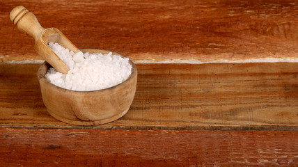 Salt or sea salt in a wooden bowl on a aged wooden table background.