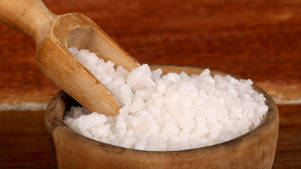 Salt or sea salt in a wooden bowl on a aged wooden table background.