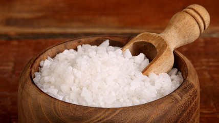 Salt or sea salt in a wooden bowl on a aged wooden table background.