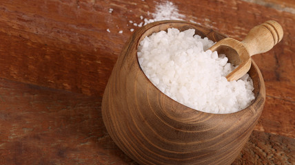 Salt or sea salt in a wooden bowl on a aged wooden table background.