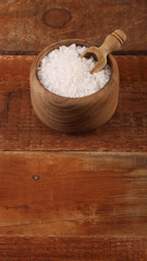 Salt or sea salt in a wooden bowl on a aged wooden table background.