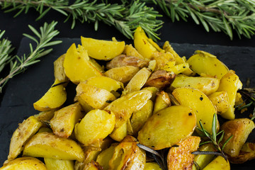 Baked potatoes with rosemary on black plate. Close-up.