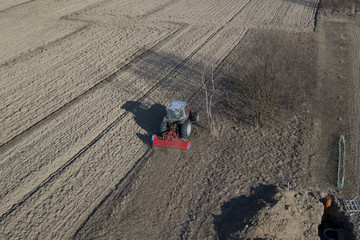 A farmer on a red tractor with a seeder sows grain in plowed land in a private field in the village...