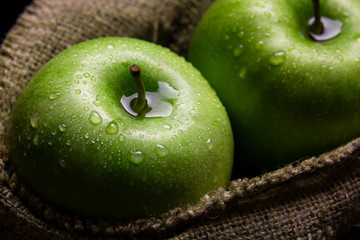 green apples in a jute bag with water drops on a dark background