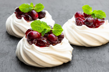 Mini Pavlova meringue nests with cranberry and mint leaves on black stone background