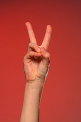 The soft hand showing the victory sign is isolated on a red background