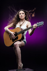 Fototapeta na wymiar Young woman with guitar, isolated on black and violet background.
