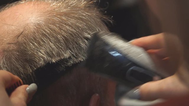 Woman Hairdresser cuts man's hair with electric clipper trimmer. Selective focus