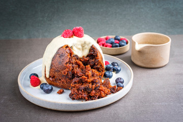 Traditional Australian plum pudding as closeup with fruits and vanilla rum sauce on a dessert plate with copy space
