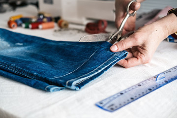 Tailor cutting jeans with scissors at workshop