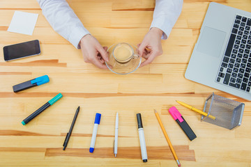 Wooden beautiful table. It has a laptop, a feather, markers, a coffee cup, pencil, phone ,a gray laptop and a women's youth hand holding a baby glove. Top view with copy space.