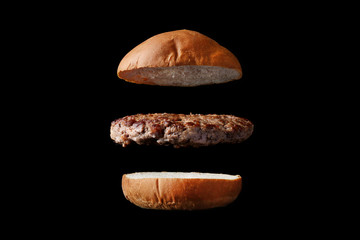 Naklejka premium flying burger with bun and patty isolated on black background