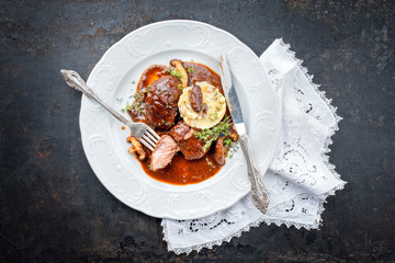 Traditional German braised pork cheeks in brown red wine sauce with mushroom and mashed potatoes as top view on a classic design white plate