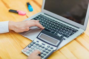 Close up of business woman holding hands with black calculator and laptop while sitting at desk in office background.