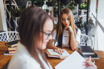 Blonde girl learning homework with her sisterin the caffe