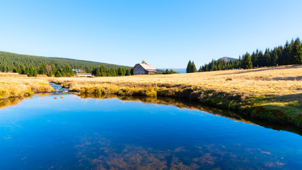 Small mountain creek meandering in the middle of meadows and forest. Sunny day with blue sky and white clouds in Jizera Mountains, Northern Bohemia, Czech Republic.
