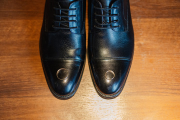 Gold wedding rings lie on the groom's shoes.