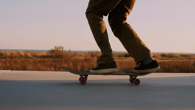 Beautiful inspirational cinematic frame of cool and trendy millennial generation z skateboarder young man, push skateboard on promenade in california beach. Amazing sunset moody light