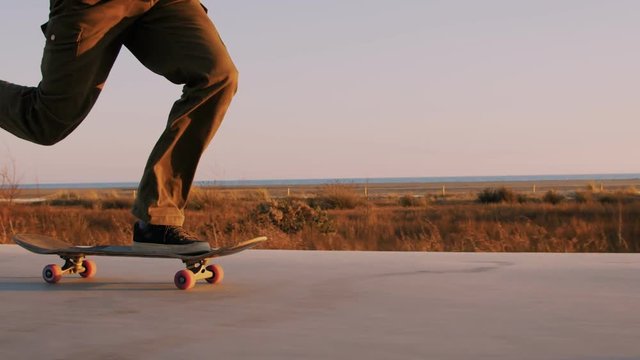 Close up of follow shot of teenage professional skateboarder move on beach promenade between people, forever young and free. Summertime sunset adventure concept. inspirational video