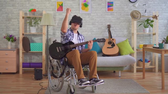 Young man disabled musician in a wheelchair and virtual reality glasses playing guitar