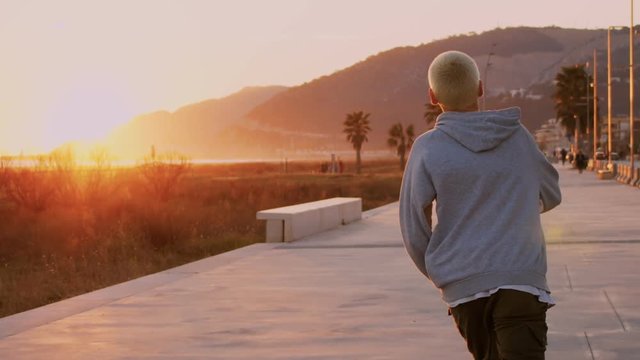 Dreamy and inspirational slow motion shot of young generation z skateboarder ride away into incredible sunset on skateboard or longboard. Moody california atmosphere or vibe