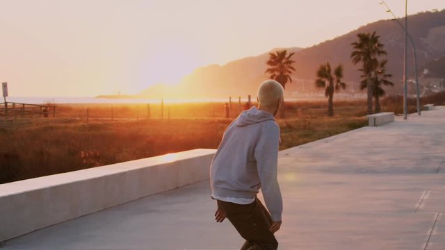 Amazing epic inspirational shot of young cool hipster millennial skateboarder ride into orange sunset on beautiful empty palm beach, california summer vibes, wanderlust adventure mood