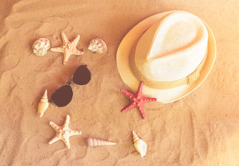 Fototapeta na wymiar Hat, sunglasses, starfishes and seashells on sand beach in sunny day.