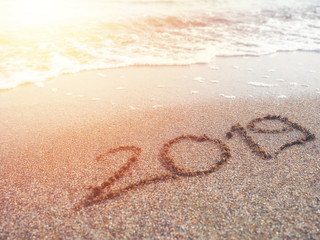 Year 2019 hand written on sandy beach in sunset warm lens flare