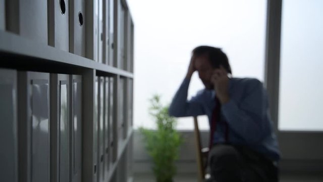 Lawyer talking on mobile phone in law office, looking edgy and panicky, selective focus on shelf with ring binders