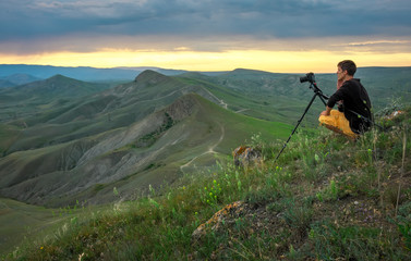 Professional photographer using a tripod, taking a photo of a mountain landscape at sunset