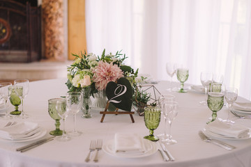 Coziness and style. Modern event design. Table setting at wedding reception. Floral compositions with beautiful flowers and greenery, candles, laying and plates on decorated table.