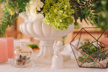 Coziness and style. Modern event design. Table setting at wedding reception. Floral compositions with beautiful flowers and greenery, candles, laying and plates on decorated table.