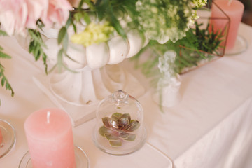 Coziness and style. Modern event design. Table setting at wedding reception. Floral compositions with beautiful flowers and greenery, candles, laying and plates on decorated table.